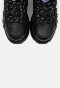 Svarta sneakers med en slät läderyta, texturerad gummisula och randiga skosnören. Rundad tå och vadderad krage för stöd.