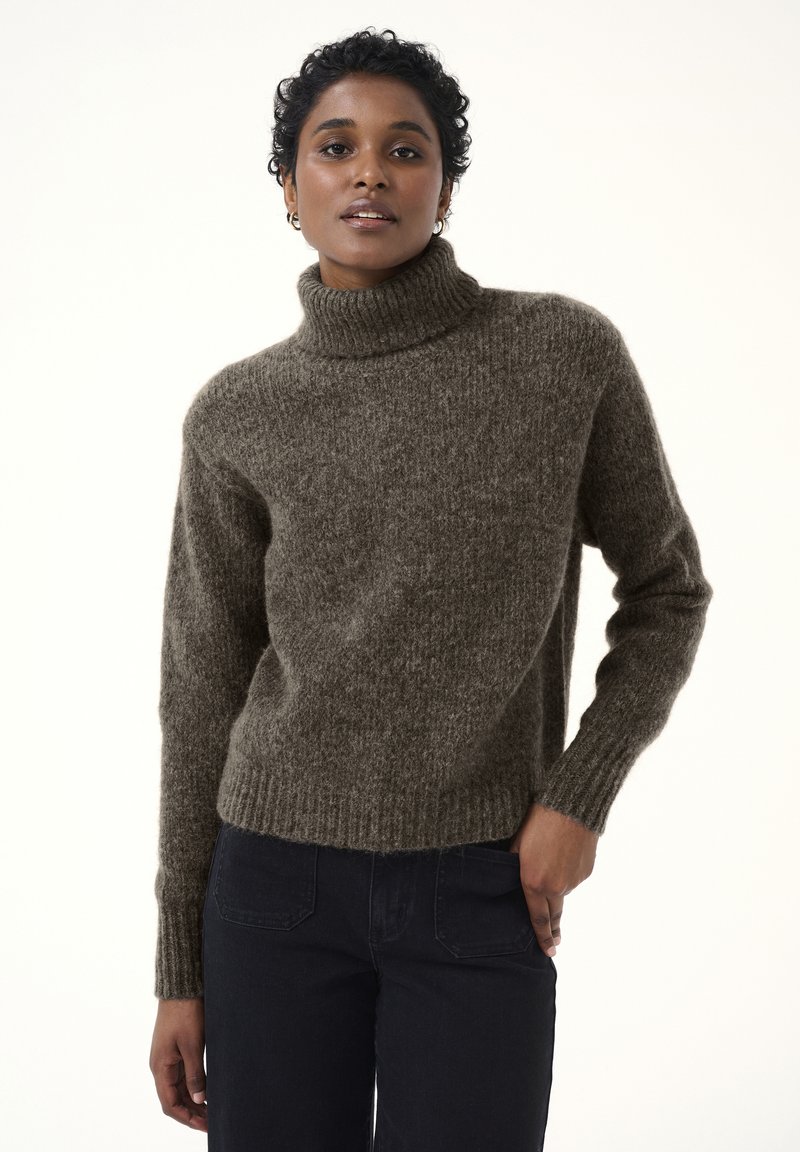 Brauner Strick-Turtleneck-Pullover mit gerippten Bündchen und Saum, der ein strukturiertes Finish aufweist. Kombiniert mit dunklen Jeans.