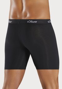 Black boxer shorts with an elastic waistband featuring the s.Oliver logo. The fabric appears smooth and fitted, highlighting leg contours.