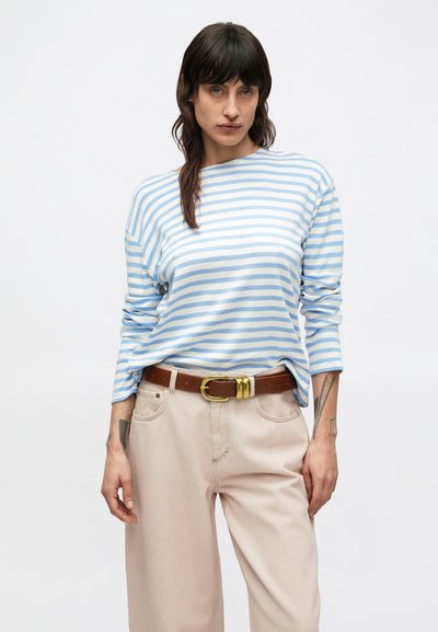 Πουκάμισο με μακριά μανίκια, ανοιχτό μπλε και λευκές ρίγες, με στρογγυλή λαιμόκοψη, συνδυασμένο με ψηλόμεσο, καφέ παντελόνι και καφέ ζώνη με χρυσή αγκράφα.