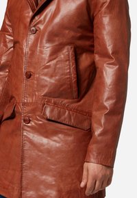 Bruine leren jas met een soepele textuur, twee knopen, zijzakken en een middellange ontwerp.