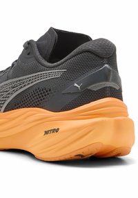Scarpa da corsa grigia con tomaia in mesh testurizzata, intersuola in schiuma arancione e dettagli argentati. Nota il logo Puma sul tallone.