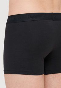 Schwarze Boxershorts aus Bio-Baumwolle mit einem weichen, elastischen Bund, der den Markennamen "Organic Basics" in einem subtilen, tonalen Muster zeigt.