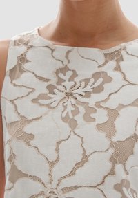 Vit ärmlös klänning med blommig spetstyg och beige inslag, rundhalsig krage och detaljerad utsmyckning genom hela tyget.