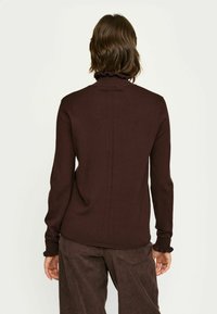 Pruunist lõngast kootud särk, millel on rippuv kaelus ja pikad varrukad, tagaküljel seamanähtud detail ja sile tekstuur. Kombineeritud pruunide sametpükstega.