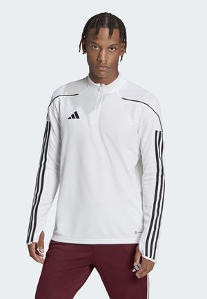 Witte sporttop met een ritskraag, zwarte strepen langs de mouwen en gestructureerde schouderpanelen. Gemaakt van lichtgewicht, ademend materiaal.