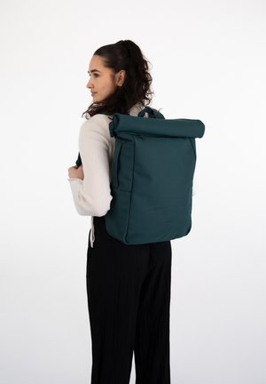 Rucsac verde cu capac tip roll-top, realizat dintr-un material durabil, dotat cu fermoare laterale, mânere duble și un design structurat. Estetică minimalistă.