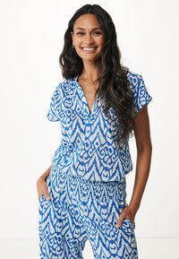 Camicia a maniche corte blu e bianca con un motivo fantasia, abbinata a pantaloni coordinati con una cintura elastica.