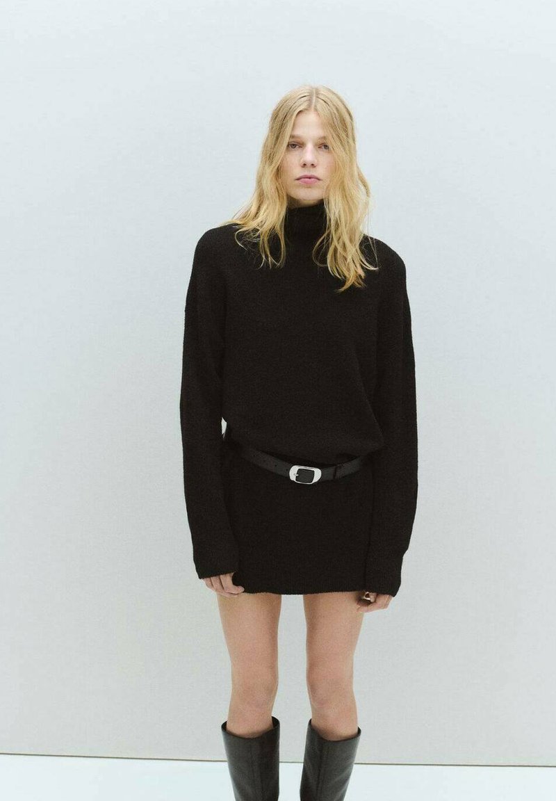 Crna pletena haljina sa visokim ovratnikom, dugim rukavima i pojasom u struku. Nosena s crnim čizmama do koljena. Glatka tekstura tkanine.