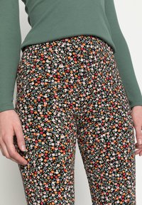 Zwarte bloemenlegging met een levendig patroon van kleine rode, witte en oranje bloemen met groene bladeren. Glad, rekbaar materiaal.