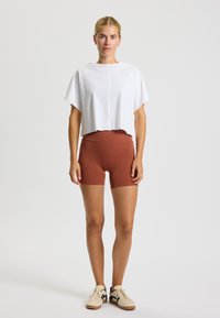 Bela skrajšana majica z ohlapnim krojem, v kombinaciji z rjavimi kratkimi hlačami z visokim pasom. Ohlapni športni čevlji dopolnjujejo videz.