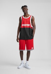 Ținută sportivă roșie și neagră, cu un tricou fără mâneci, având text îndrăzneț "STARTER", asortată cu șorturi roșii și adidași albi.