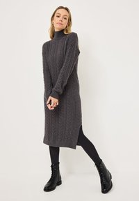 Grå kabelstrikket sweaterkjole med høj hals, lange ærmer, sideslids og ribbet kant, parret med sorte ankelstøvler med snørebånd.