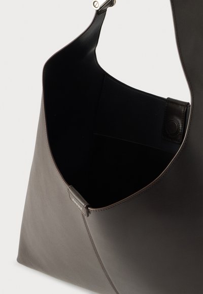 Sac à bandoulière en cuir brun foncé avec une large sangle, ouverture supérieure et fermeture à bouton-pression magnétique à l’intérieur.