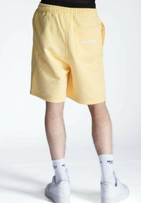 Pantalones cortos amarillos de tela suave con una cinturilla elástica, que cuentan con un bolsillo trasero y un pequeño logotipo en blanco.