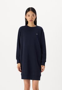 Abito felpa blu navy realizzato in materiale morbido, con scollatura rotonda, maniche lunghe e un piccolo logo sul petto. Vestibilità comoda.