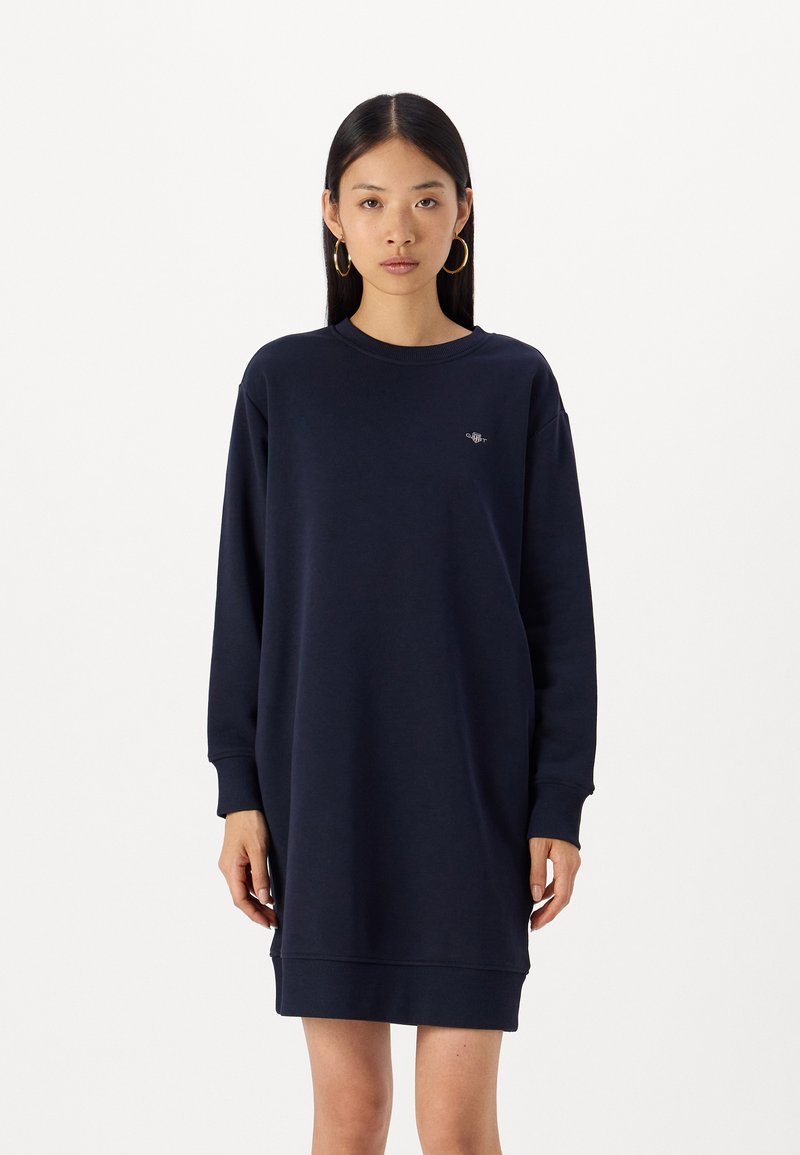 Abito felpa blu navy realizzato in materiale morbido, con scollatura rotonda, maniche lunghe e un piccolo logo sul petto. Vestibilità comoda.