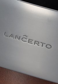Metaliczna srebrna powierzchnia z wytłoczonym logo "LANCERTO" z zakrzywionym akcentem na literze "N", na tle teksturowanym w odcieniach brązu.