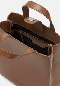 Brązowa skórzana torebka z dwoma uchwytami, zapięciem na zatrzask i kieszonką na zamek. Wnętrze ma czarne podszycie i tłoczone logo.