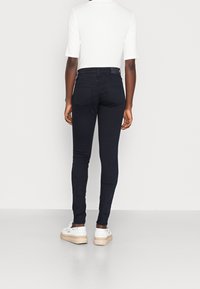 Jeans ajustados negros confeccionados en material elástico, con cintura alta y dos bolsillos traseros. Combinados con zapatillas blancas y mangas cortas.