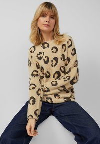 Beige trui met een zachte textuur, voorzien van een luipaardprint in zwart en bruin. Losse pasvorm met lange mouwen, gecombineerd met donkerblauwe spijkerbroek.