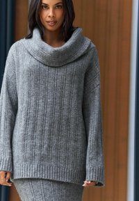 Grauer Strickpullover mit einem Schalkragen, der ein vertikales Rippmuster und lange, weite Ärmel aufweist. Weiches Material mit lockerer Passform.
