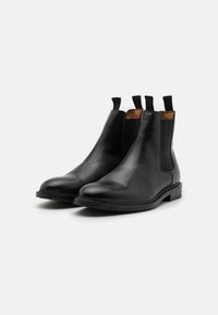 Botas Chelsea negras de cuero con paneles laterales elásticos, punta redonda y tiradores, que cuentan con una suela de goma plana y una textura lisa.