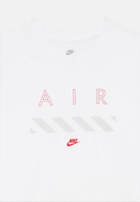 Weißes T-Shirt mit dem Wort "AIR" in roten Buchstaben und einem grauen diagonalen Streifenmuster, mit einem kleinen roten Nike-Logo am unteren Ende.