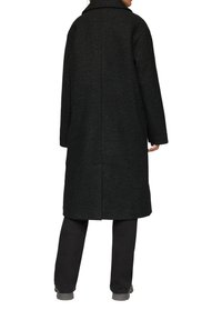Zwarte wolmixjas met een gestructureerde afwerking, met een lange, rechte silhouet, brede kraag en zijzakken. Gedraaid over zwarte broek.