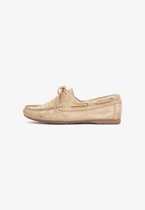 Mocassin beige en suède avec fermeture à lacets, œillets métalliques, pointe cousue et détail de laçage latéral, présenté de profil sur fond blanc.