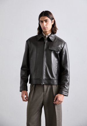 Veste en cuir noir avec un col, fermeture éclair à l'avant et une poche sur la poitrine. Elle dispose de poches latérales et d'une coupe courte.