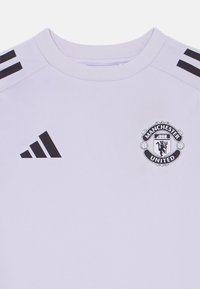Lys lilla kortermet skjorte med svarte striper på skuldrene og Manchester United-logo. Laget av et glatt, pustende stoff.