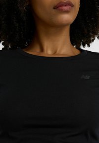 Schwarzes, geripptes T-Shirt mit kurzen Ärmeln und rundem Halsausschnitt; verfügt über ein dezentes graues Logo auf der linken Seite. Weicher, texturierter Stoff.