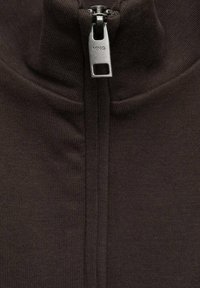 Giacca in pile marrone scuro con zip, dotata di colletto alto, caratterizzata da una zip metallica e texture a coste lungo le cuciture.