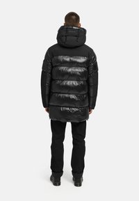 Svart puffjacka med horisontellt kviltat mönster, glänsande ytfinish och huva. Bärs över svarta byxor och stövlar. Slät textur, medellång design.