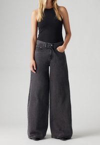 Szerokie czarne dżinsy z wysokim stanem, z regulowanym ściągaczem, dużymi kieszeniami i lekko postarzanym wykończeniem.