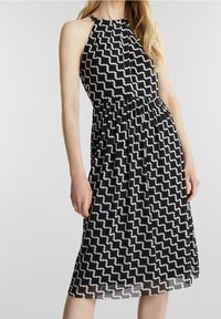 Robe noire et blanche à col halter présentant un motif de nuages ondulés, taille cintrée et tissu fluide tombant sous le genou.