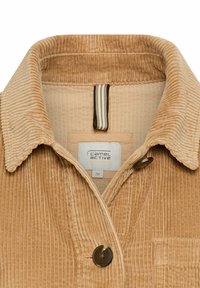 Karamelkleurige corduroy shirt met een kraag, drie-knopen sluiting, een voorzak en een geweven label met merk- en maatgegevens.