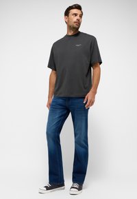 Camiseta gris de manga corta con cuello redondo, combinada con jeans azules. La camiseta tiene un pequeño logo en el pecho, ajuste casual, material de algodón.