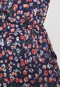 Granatowa tkanina z kwiatowym wzorem w odcieniach różowego, białego i zielonego. Posiada falbaniasty dekolt oraz detal związany w talii.