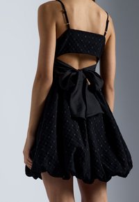 Robe noire avec un motif à carreaux texturé, fines bretelles, dos nu et un grand nœud à la taille, dotée d'une jupe évasée.