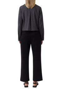 Szary skórzany żakiet z plisowanym tyłem, w połączeniu z czarnymi spodniami o szerokich nogawkach i czarnymi sandałami. Materiały wydają się gładkie i dopasowane.