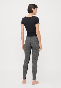 Svart kortärmad topp som matchas med mönstrade svarta och vita leggings. Leggings har en geometrisk design och en figurnära silhuett.