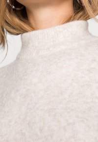 Beige, hoogsluitende, wollen trui met een zachte textuur en subtiele kleurvariaties, die een schoon en minimalistisch ontwerp tentoonstelt.
