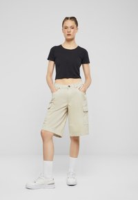 Beige cargoshorts med sidelommer, laget av bomull og med rett snitt. Kombinert med en tettsittende svart crop top og hvite sneakers med ankel sokker.