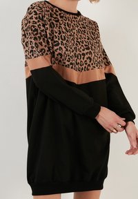 Černé šaty-sweatshirt s leopardím potiskem v horní části, s béžovým pruhem a černými rukávy. Měkká, texturovaná tkanina s žebrovanými manžetami.