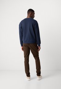 Navy blue sweatshirt with ribbed neckline, paired with dark brown slim-fit pants and light beige sneakers, viewed from the back.