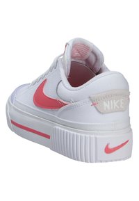 Baskets Nike blanches avec un swoosh et des accents roses, présentant un dessus texturé, une semelle épaisse et une collerette rembourrée.
