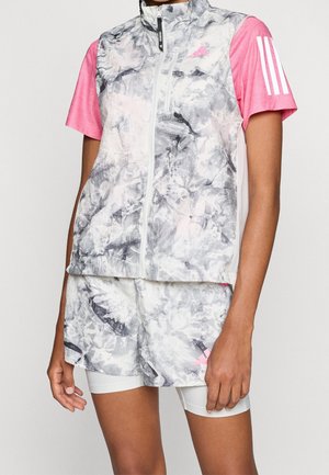 Sportovec nosící šedou mramorovou vesta bez rukávů na zip a šortky přes bílé kompresní šortky, s růžovým tričkem s krátkým rukávem, na kterém jsou tři bílé pruhy.