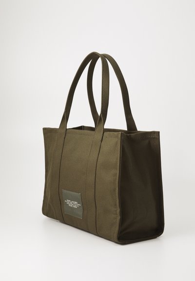 Torebka typu tote w oliwkowym kolorze, wykonana z mocnej tkaniny, z dwiema rączkami, prostokątnego kształtu, z małą prostokątną metką z przodu.